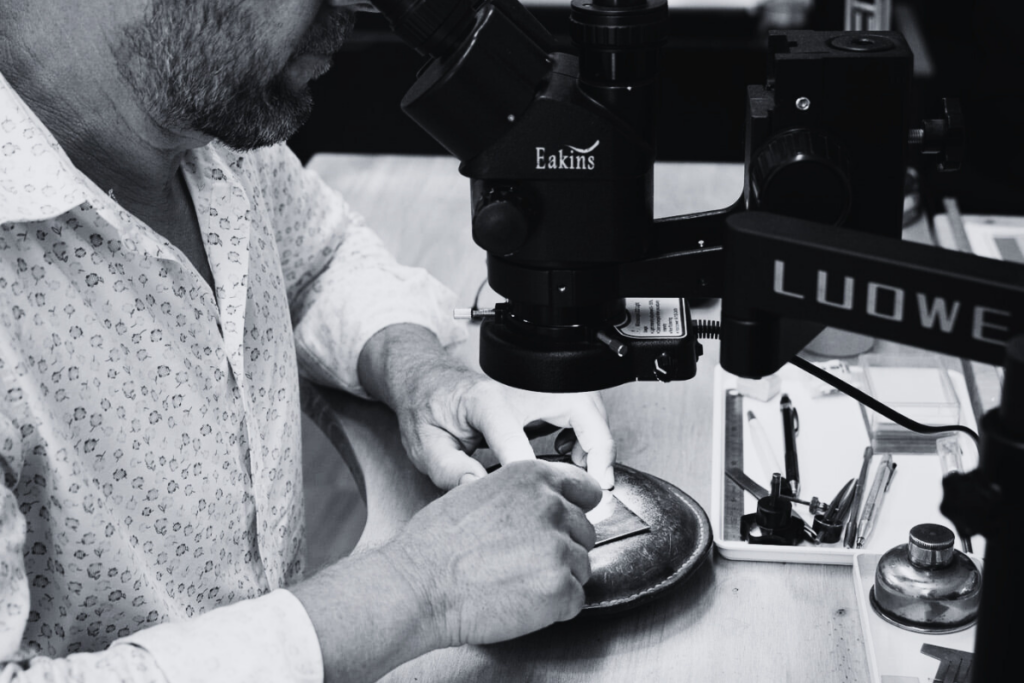 Eric Leroy - graveur main et meilleur Ouvrier de France concentré utilisant une loupe binoculaire pour une gravure héraldique manuelle dans l’atelier Art Gravure