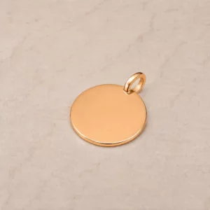 Médaille ronde en or jaune massif avec bélière intégrée, surface lisse prête à la gravure, fabrication artisanale à Tours.